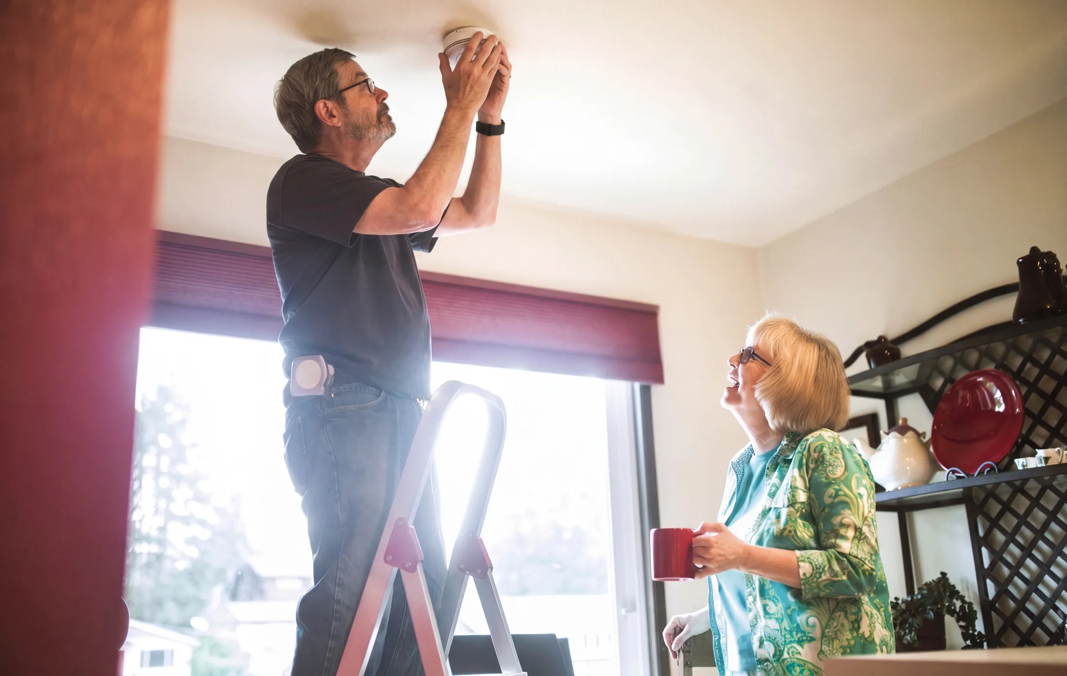 Homeowner installing a wireless smoke alarm indoors